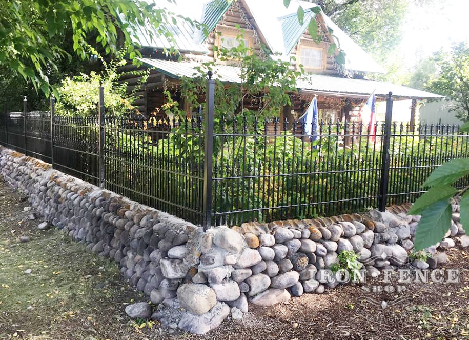 A Custom-Built Wrought Iron Fence with Puppy Pickets and Fleur De Lis Finials on a Rock Wall