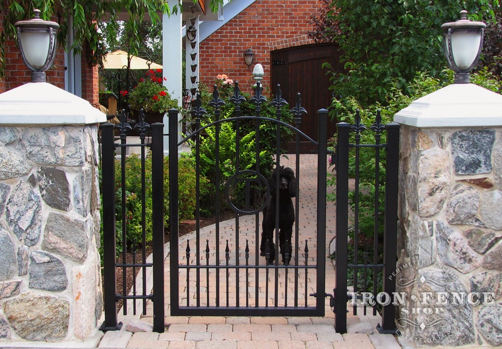 Custom iron walk gate with integrated initial and puppy pickets mounted between stone columns (Style #15 - Puppy Picket Finials)