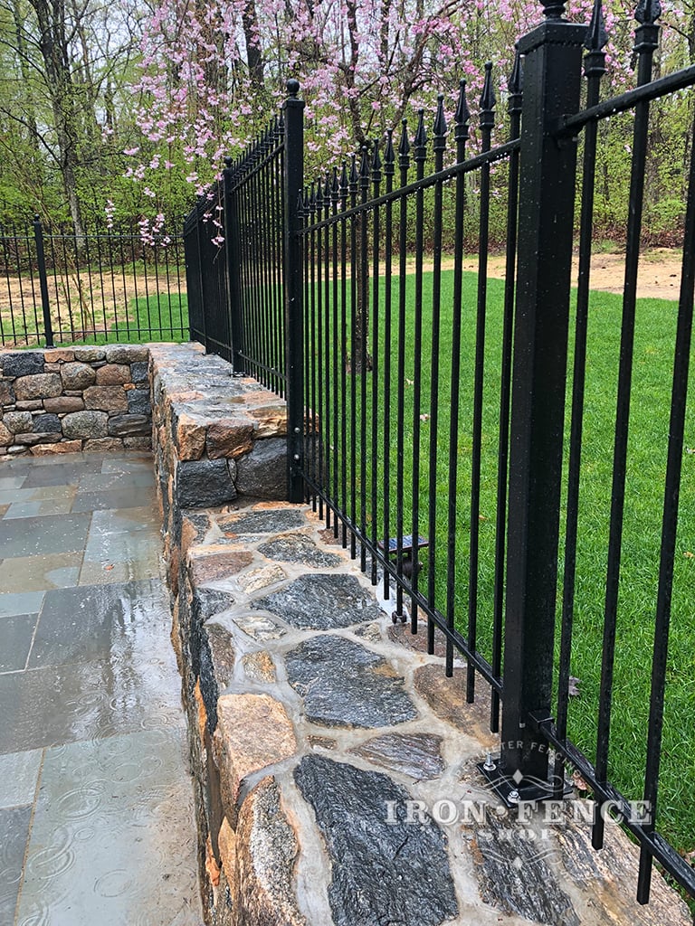 An Iron Fence Installed Stair-Step Style Down a Stone Wall Top