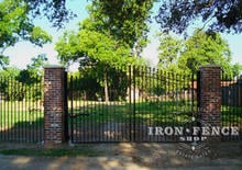 Custom height iron arched driveway gate with triad finials mounted between brick pillars